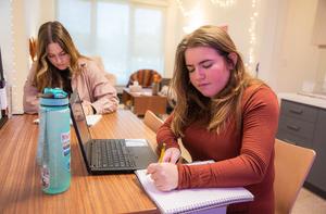 Two students work on homework together at a kitchen table area.